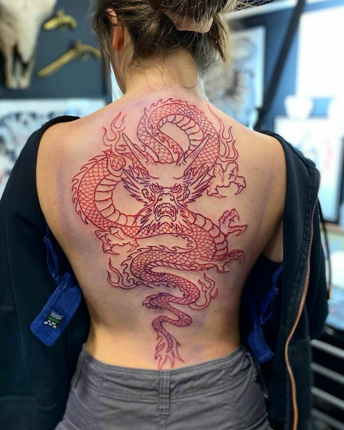 Woman with a large red ink tattoo of a dragon on her back at a tattoo studio.