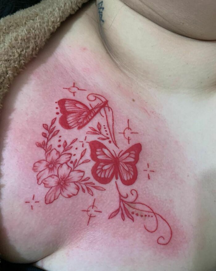 Red ink tattoo of butterflies and flowers on skin, showing delicate and intricate design details.