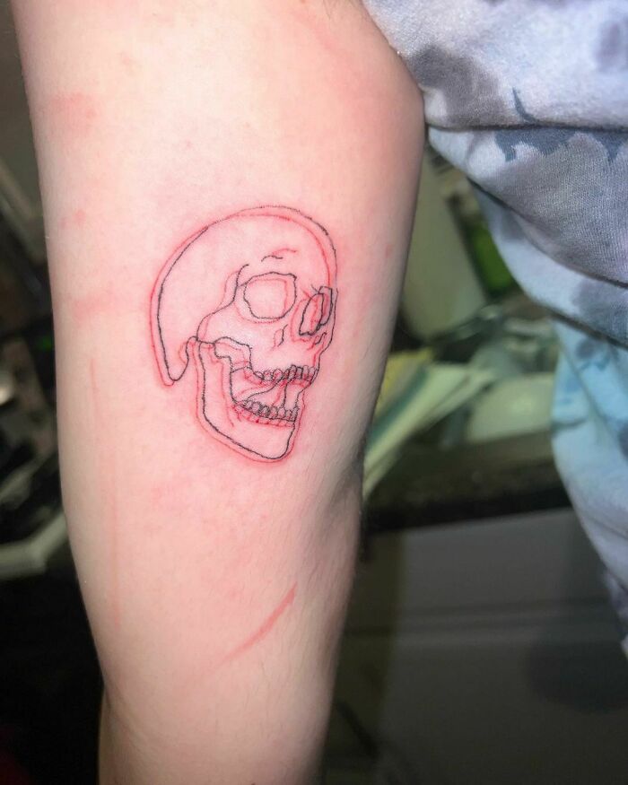 Red ink tattoo of a skull on an arm, showcasing intricate line work in a minimalist style.