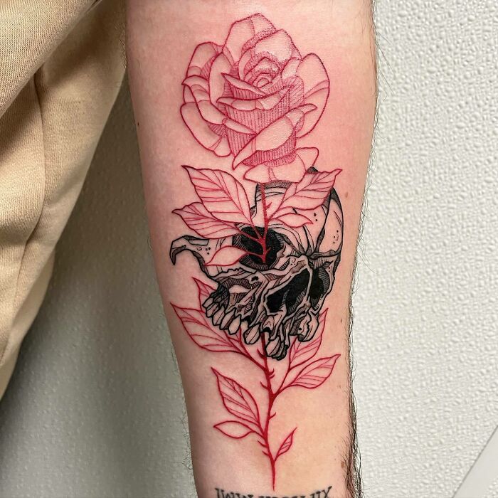 Red ink tattoo featuring a rose and skull on forearm, showcasing intricate design elements.