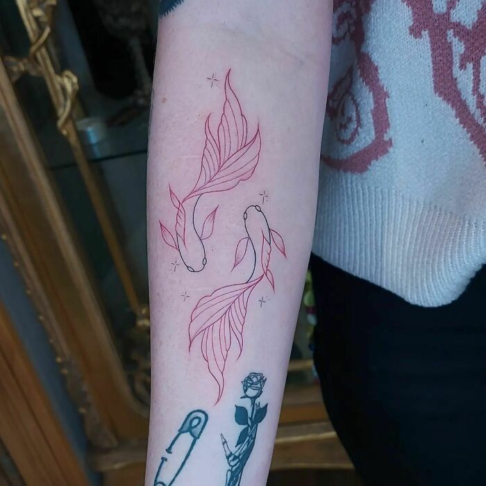 Red ink tattoo of two koi fish on forearm, showcasing elegant design and intricate linework.