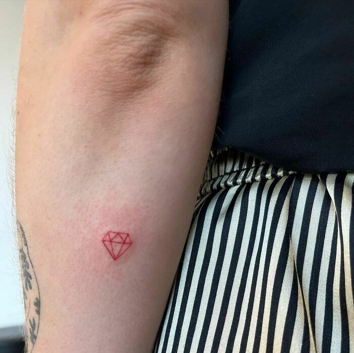 Red ink tattoo of a geometric diamond on an arm.