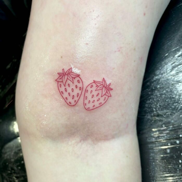 Two strawberries in red ink tattoo design on forearm.