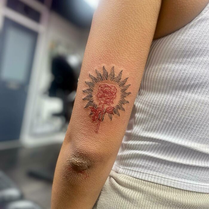 Red ink tattoo of a floral sun design on forearm, showcasing intricate details and vibrant color.