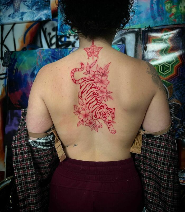 Person with a red ink tattoo of a tiger and flowers on their back.
