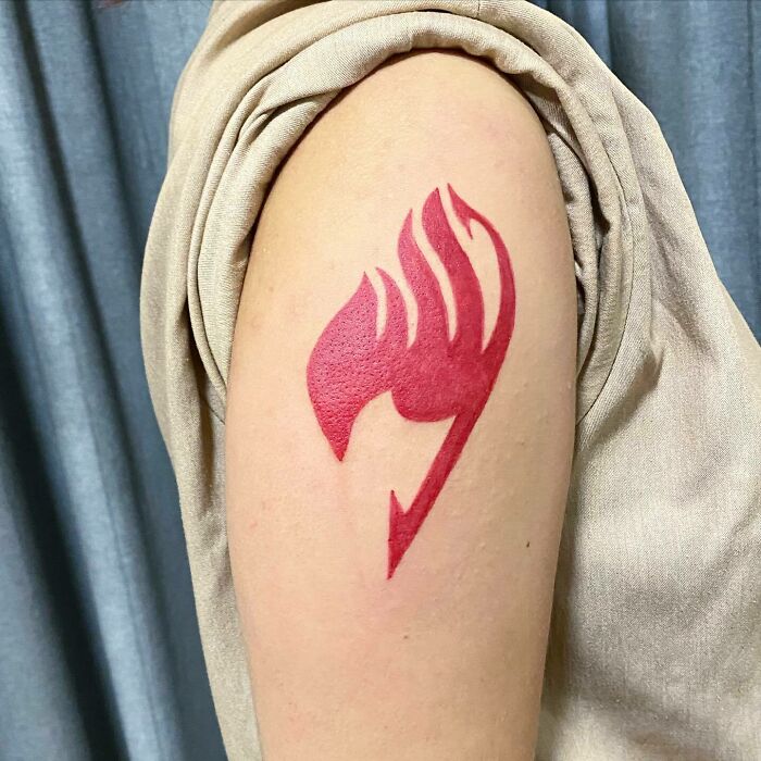 Red ink tattoo of a stylized flame design on an upper arm.