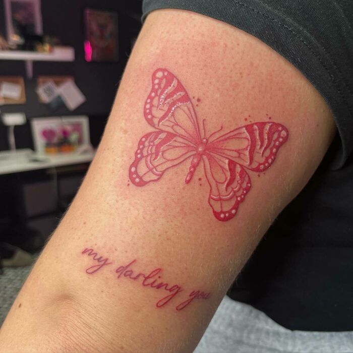Red ink butterfly tattoo with "my darling you" text on a person's arm.