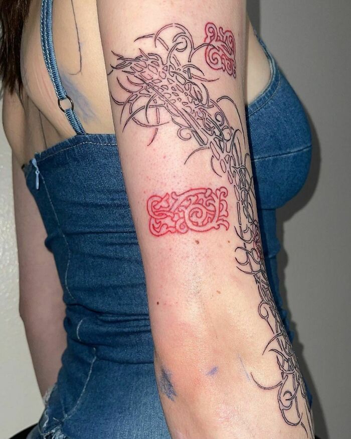 Red ink tattoo design on a person's arm, featuring intricate patterns and details in a denim top.