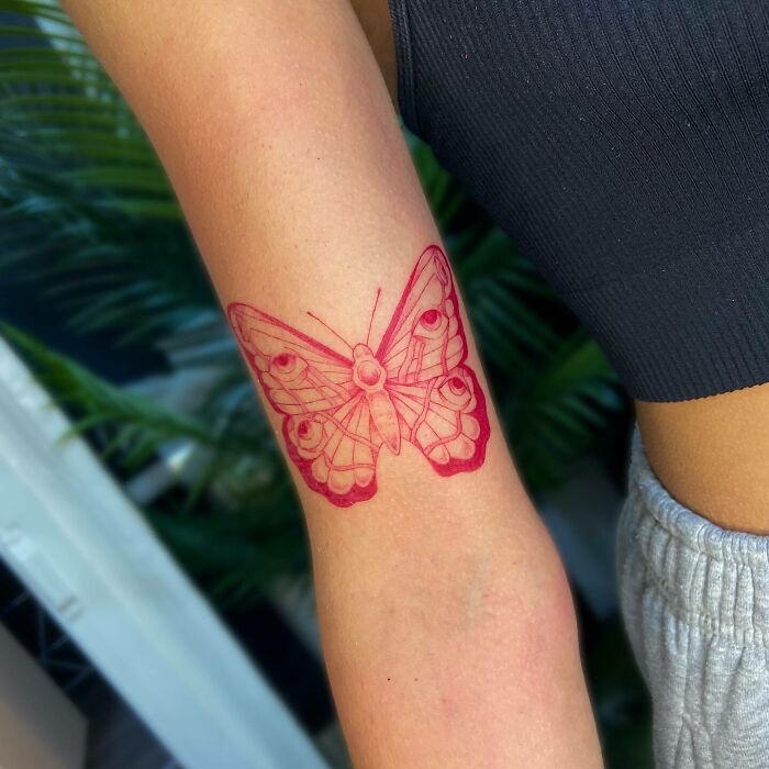 Red ink butterfly tattoo on arm, showcasing detailed design and vibrant color.