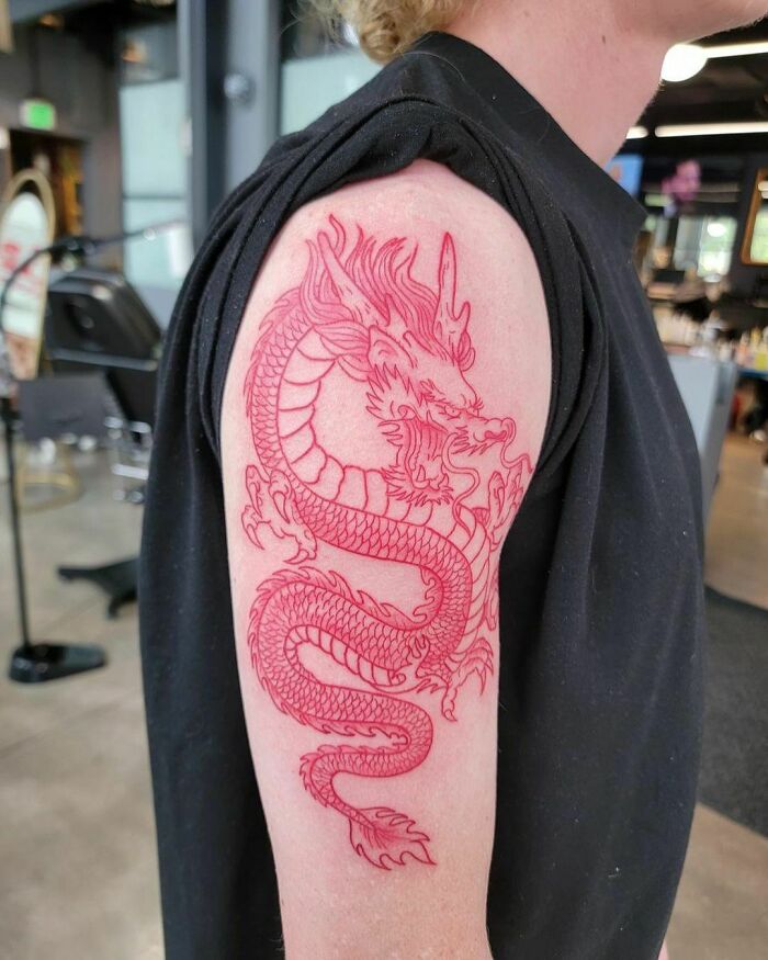 Red ink tattoo design of a dragon on upper arm in a tattoo studio setting.