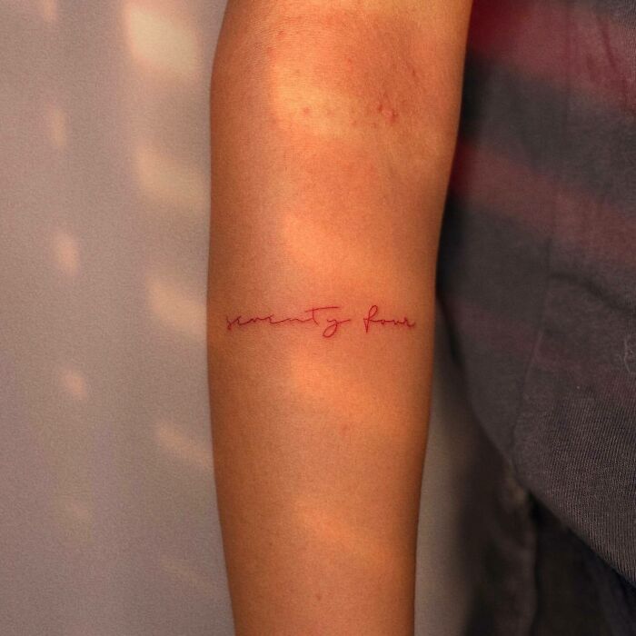 Minimalistic red ink tattoo design on a person's forearm, showcasing elegant script text.