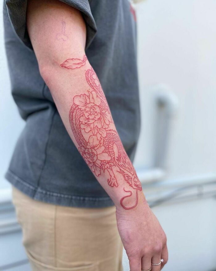 Red ink tattoo design of a dragon and flowers on a person's forearm, showcasing intricate red tattoo art.