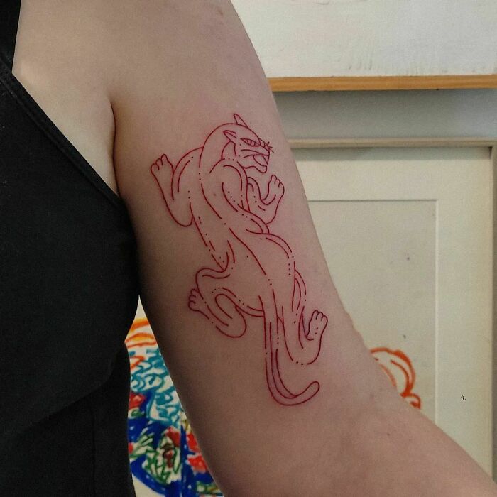 Arm with a red ink tattoo of a panther, showcasing intricate linework.