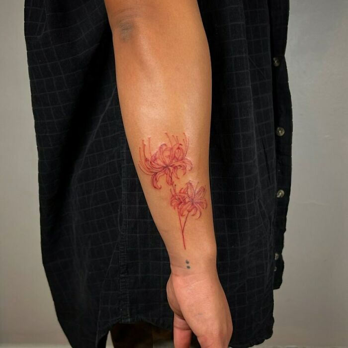 Red ink tattoo of delicate floral design on forearm, showcasing intricate details in a simple, elegant style.