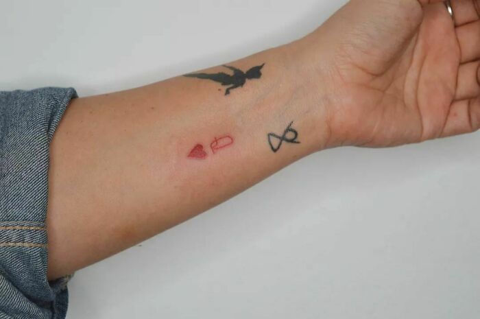 Red ink tattoo of heart and key on forearm with bird and infinity symbol.
