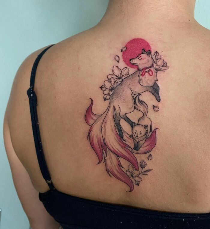 Red ink tattoo of a fox and flowers on a person's back.
