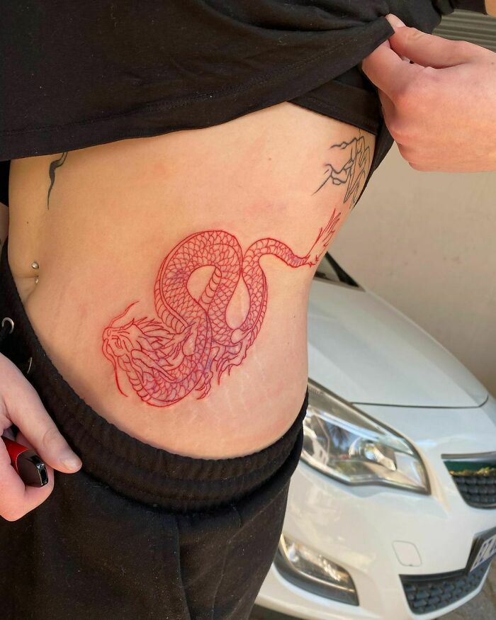 Person showcasing a red ink dragon tattoo on their side, emphasizing unique tattoo design ideas.