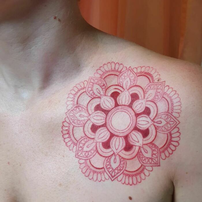 Red ink tattoo of a detailed mandala design on a person's shoulder.