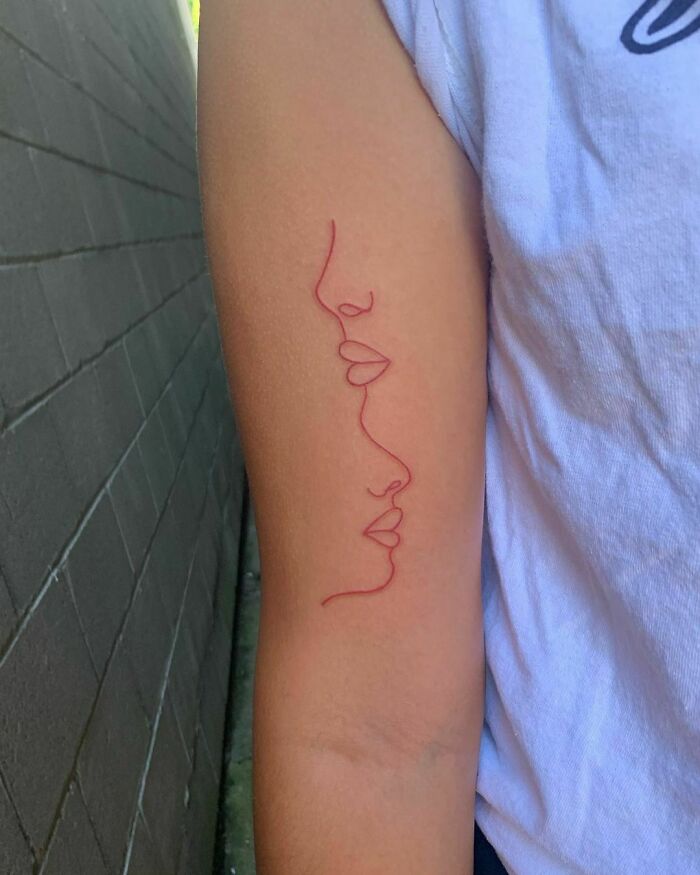 Red ink tattoo of a minimalist face design on an arm, showcasing creative tattoo ideas.