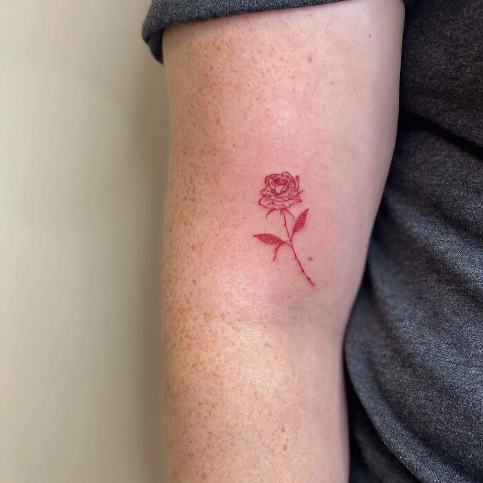 Red ink tattoo of a delicate rose on an arm, highlighting simple and elegant tattoo design.