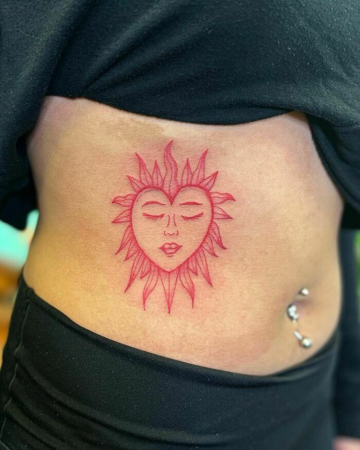Red ink tattoo of a sun with a face on a person's side.