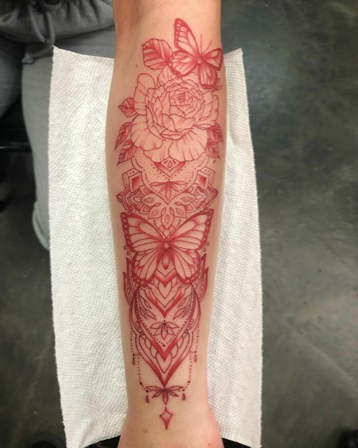 Red ink tattoo featuring intricate floral and butterfly designs on forearm.