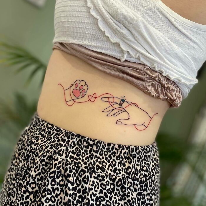 A red ink tattoo depicting a hand and a paw on a person's side, showcasing creative design ideas.
