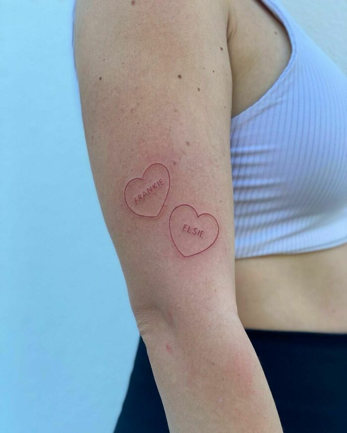 Close-up of two red ink heart tattoos labeled Frankie and Elsie on a person's arm.