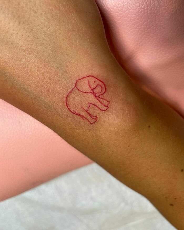 Red ink tattoo of a minimalist elephant design on an arm.