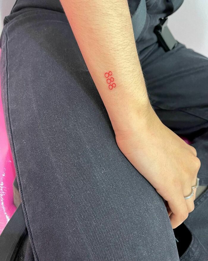 Small red ink tattoo of the number 888 on a person's forearm against a black fabric background.