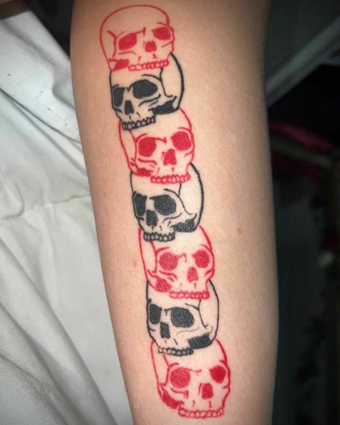 Red ink tattoo design featuring alternating red and black skulls on a forearm.