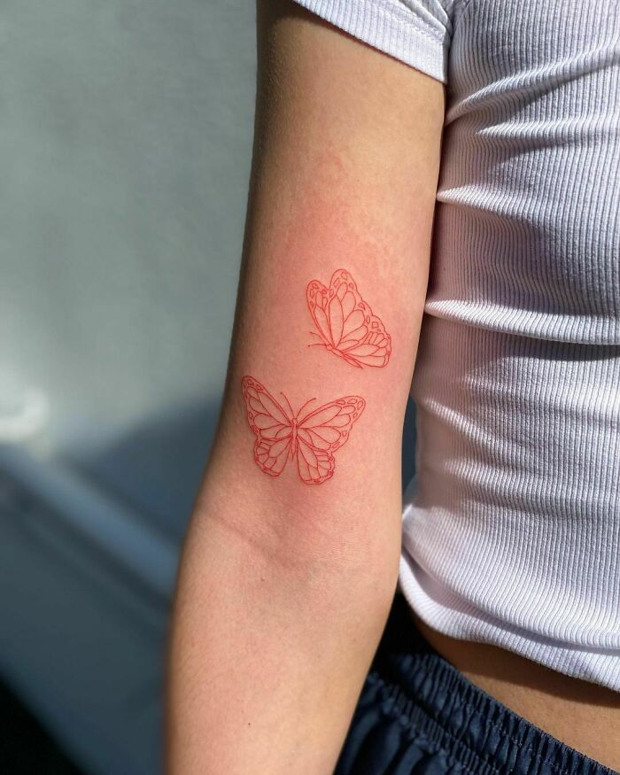 Red ink tattoo of two butterflies on a person's arm in natural light.