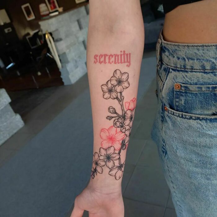 Forearm tattoo with red ink text "serenity" and floral design, showcasing red ink tattoo art.