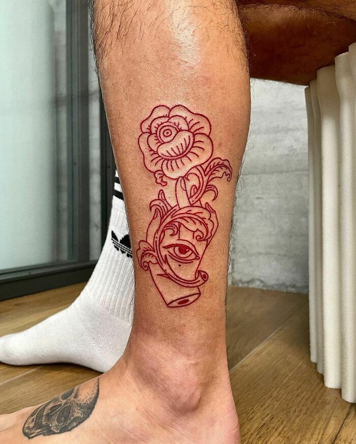 Red ink tattoo of a flower with an eye on a person's leg.