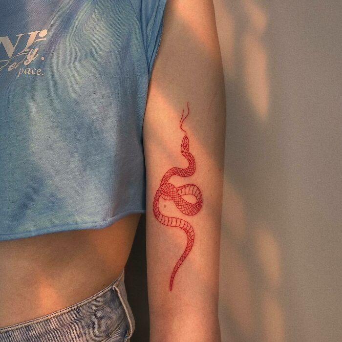 Red ink tattoo of an abstract snake design on a person's arm, wearing a blue top.