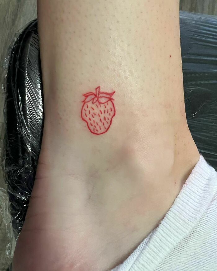 Small red ink strawberry tattoo design on ankle.