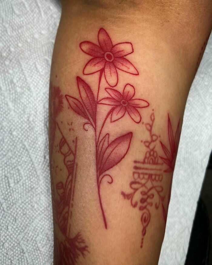Floral red ink tattoo on forearm featuring delicate flowers and leaves in a minimalist design.
