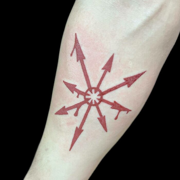 Red ink tattoo with arrow design on a forearm, showcasing intricate detailing.