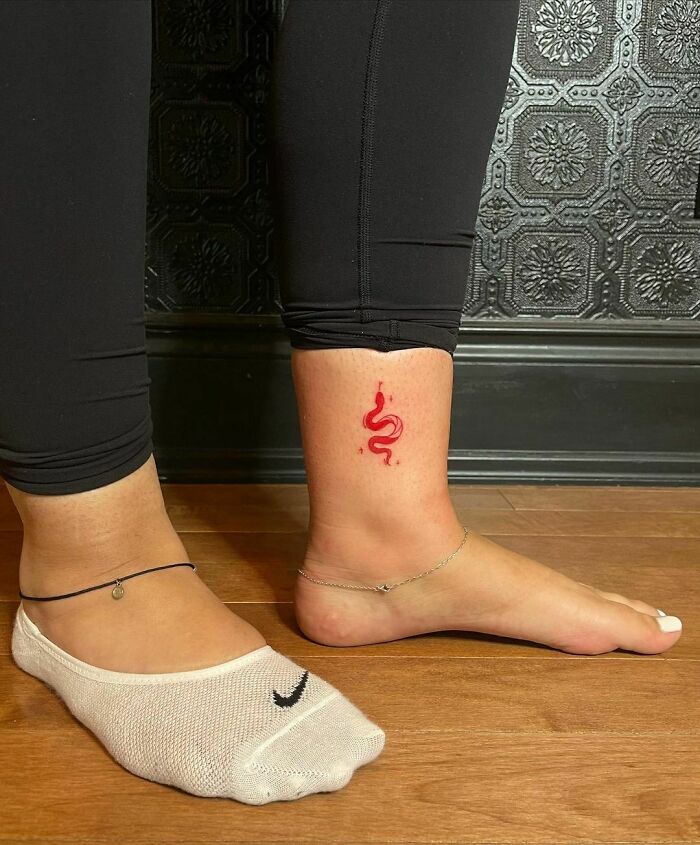 Red ink tattoo of a snake on a person's ankle, showcasing a minimalist design on the skin.