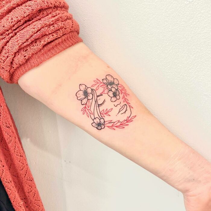 Red ink tattoo design on arm featuring floral and face elements with delicate line work.