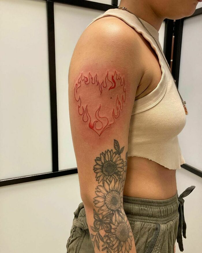 Person with a red ink tattoo of a flaming heart on their upper arm, showcasing a unique tattoo design.