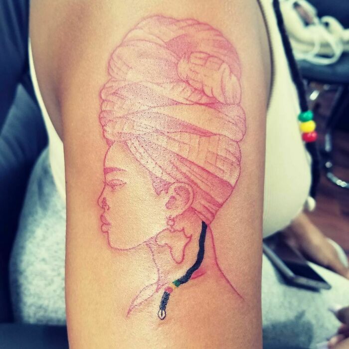 Red ink tattoo of a woman's profile with a headdress and earrings on an arm.