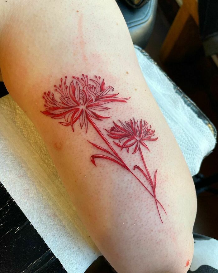 Red ink tattoo design of two detailed flowers on a person's arm.