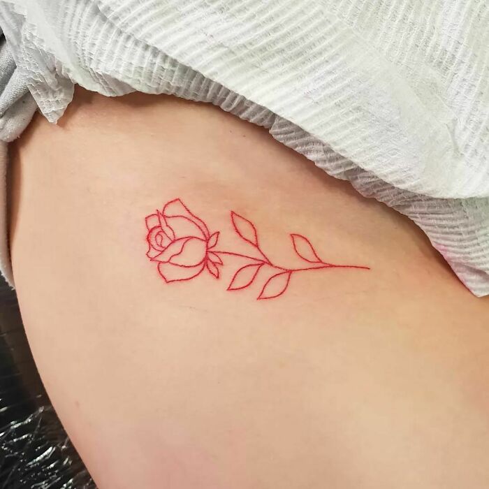 Red ink tattoo of a rose on skin, showcasing delicate linework and floral detail.