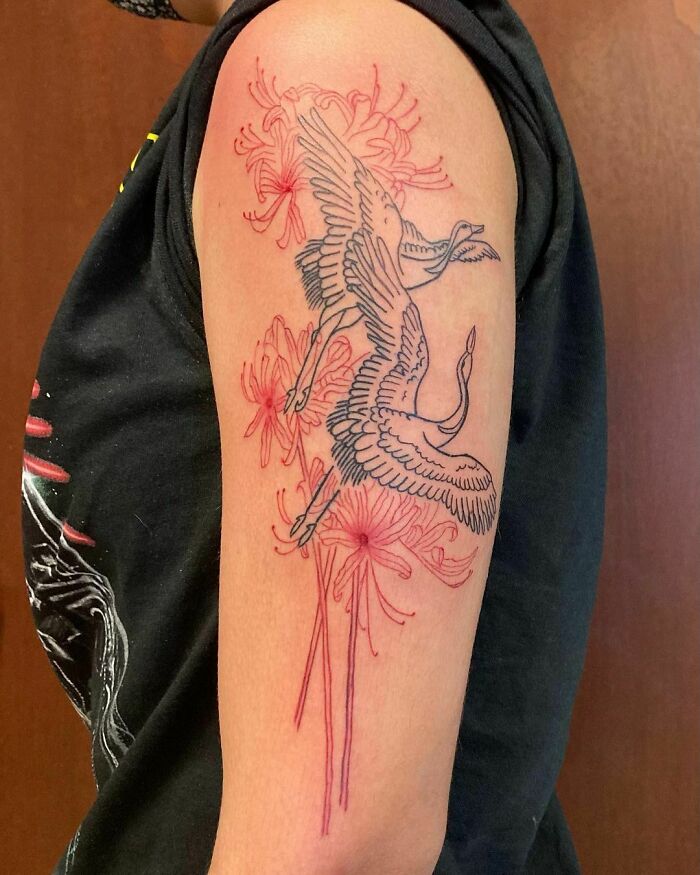 Red ink tattoo of cranes with floral accents on upper arm.