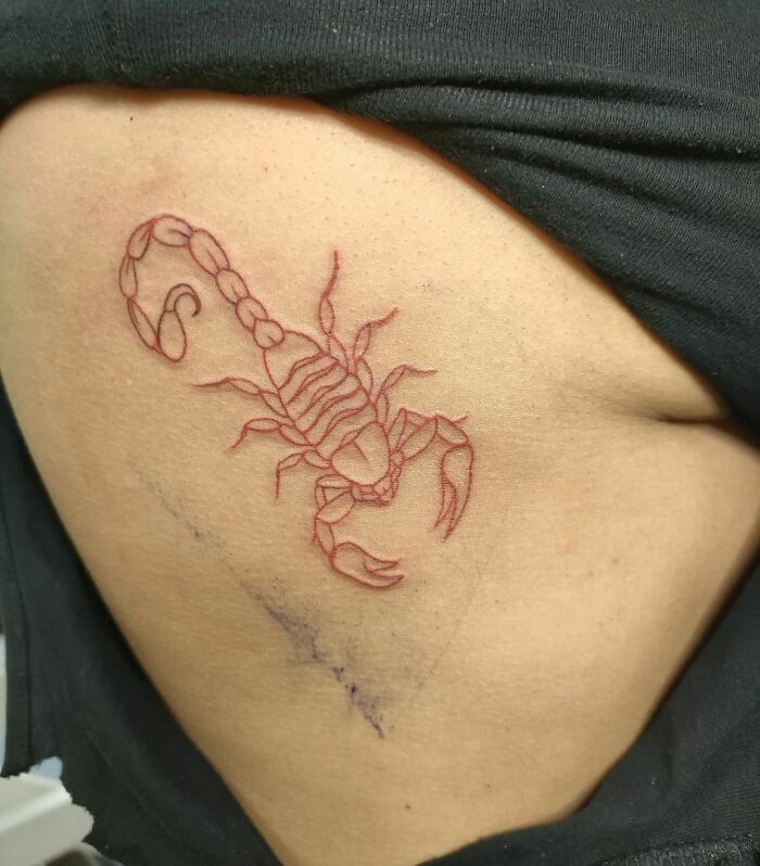 Red ink tattoo of a scorpion on skin, showcasing intricate line work and elegant design.