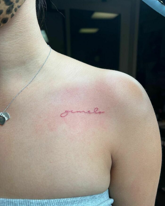 Minimalist red ink tattoo on a woman's shoulder, showcasing delicate script design.