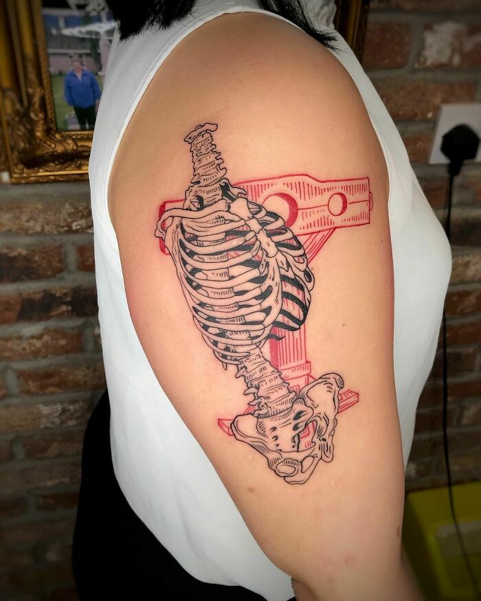 Red ink tattoo featuring an anatomical ribcage design on upper arm.