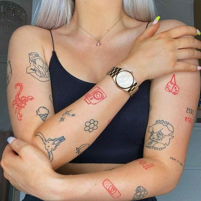 Woman with various ink tattoos, including red designs, wearing a black top and gold watch.