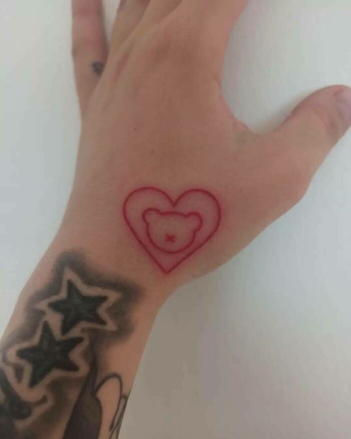 Red ink tattoo of a heart with a bear design on a hand.